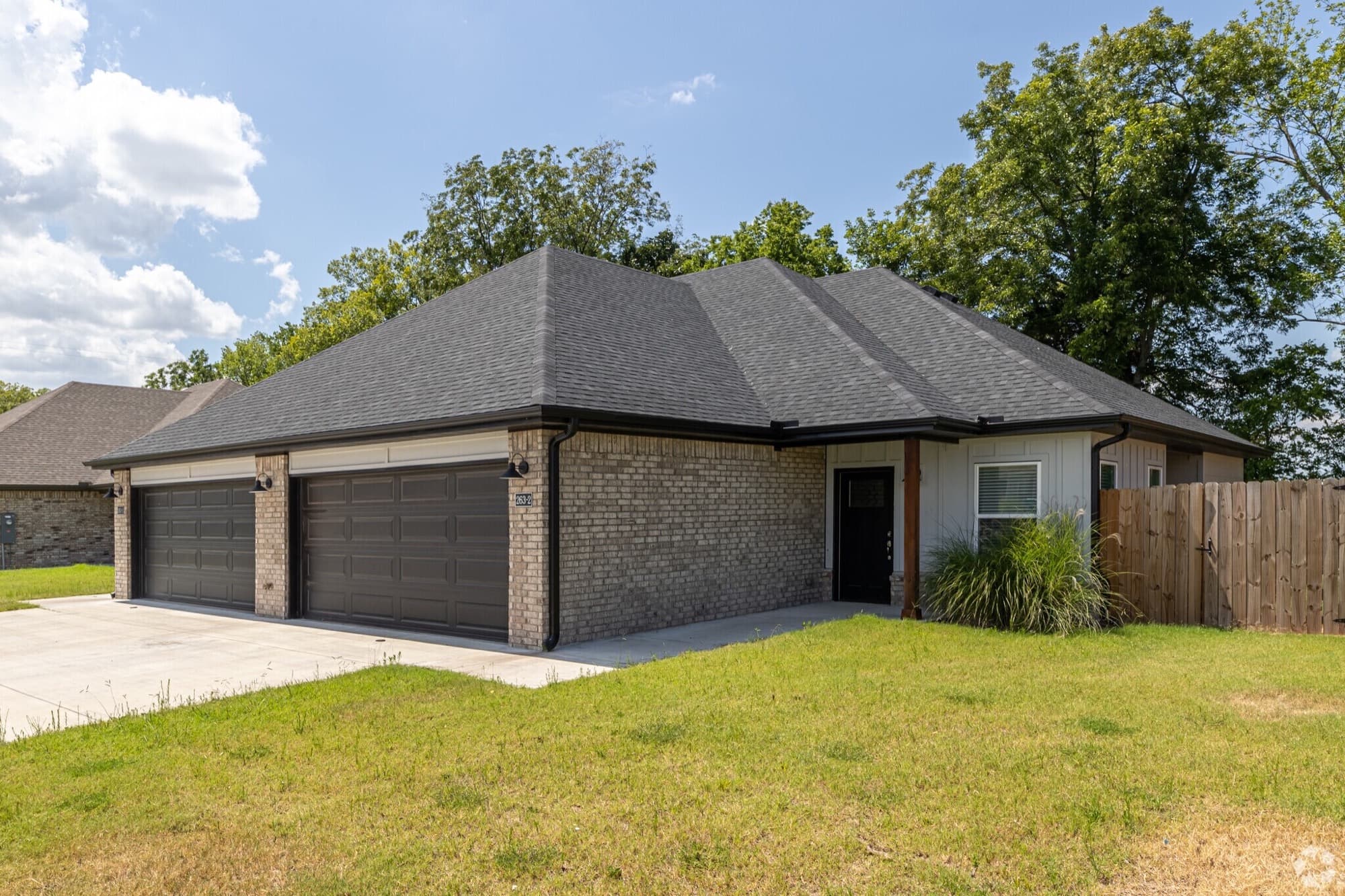 A newly built Farmington Hills duplex with brick, a two-car garage, and a green lawn under blue sky